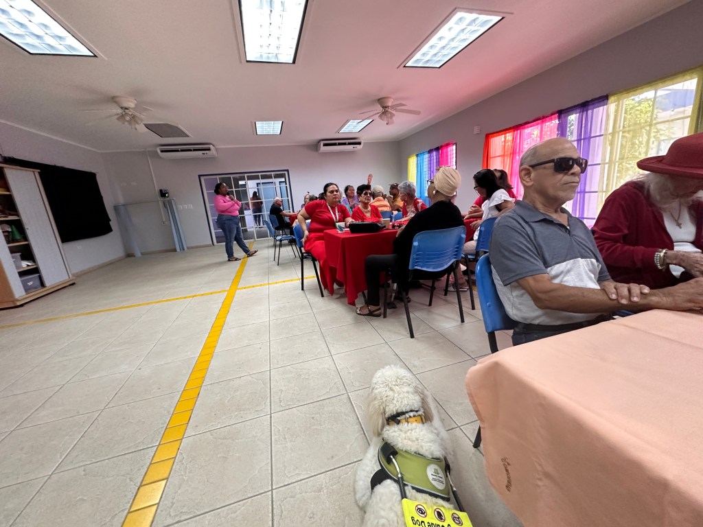 gezelligheid aan de tafels op de locatie bij Favi. Vooraanstaat een vrijwilligster met een microfoon in haar hand