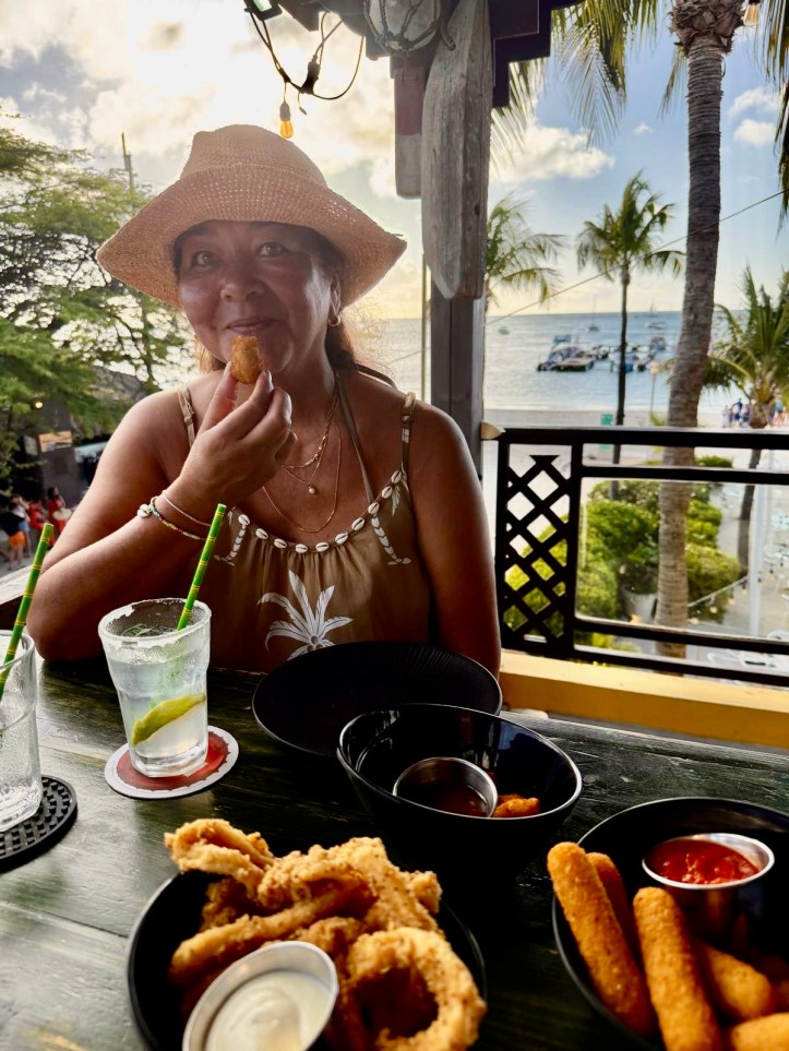 Carin met een bittergarnituurtje in de hand. op een barkruk in een beachbar